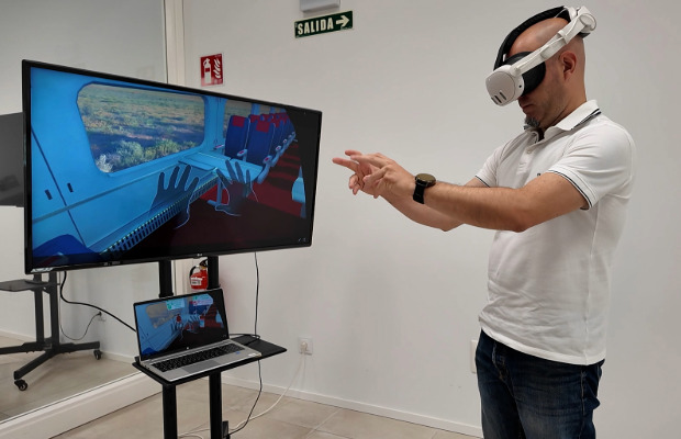 Persona usando gafas de realidad virtual y controlando con manos libres en simulador de incendios e-Xtinguisher, proyectado en pantalla.