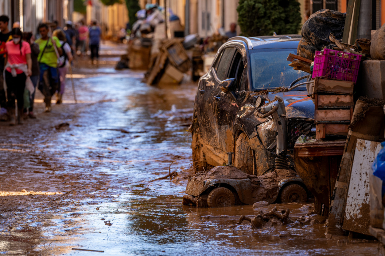 Calle inundada con coches dañados y personas caminando tras una riada