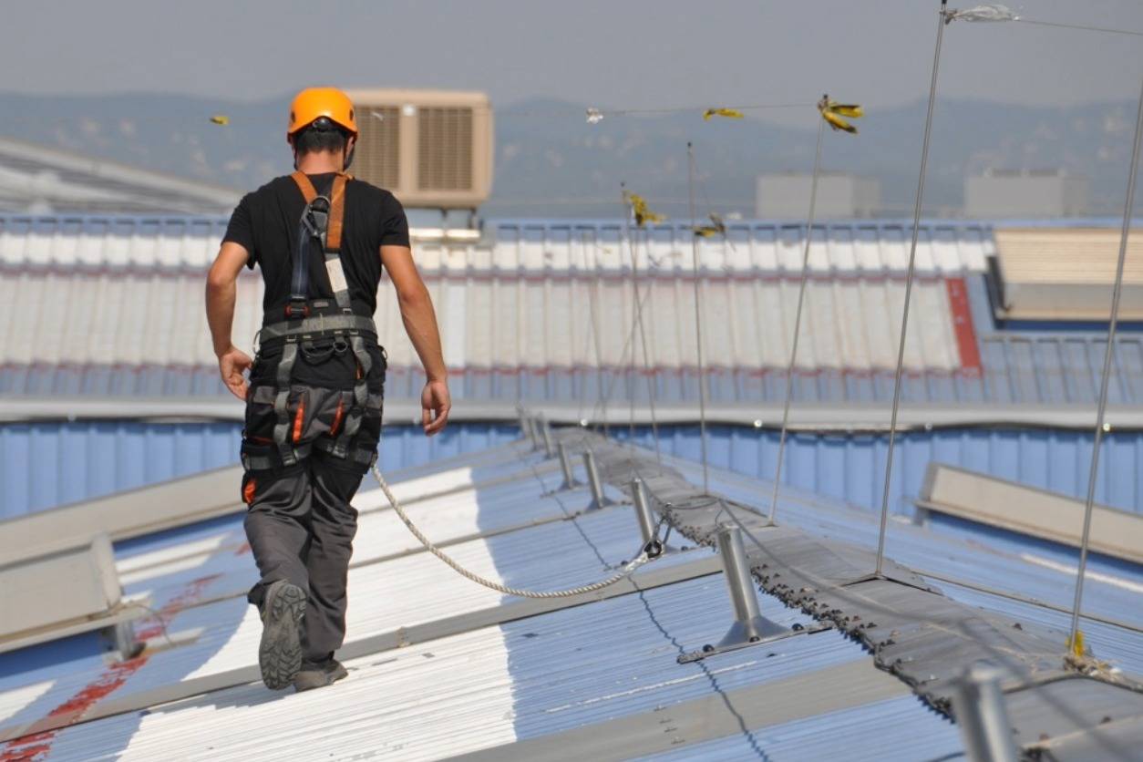 Trabajador con arnés de seguridad conectado a una línea de vida en cubierta industrial.